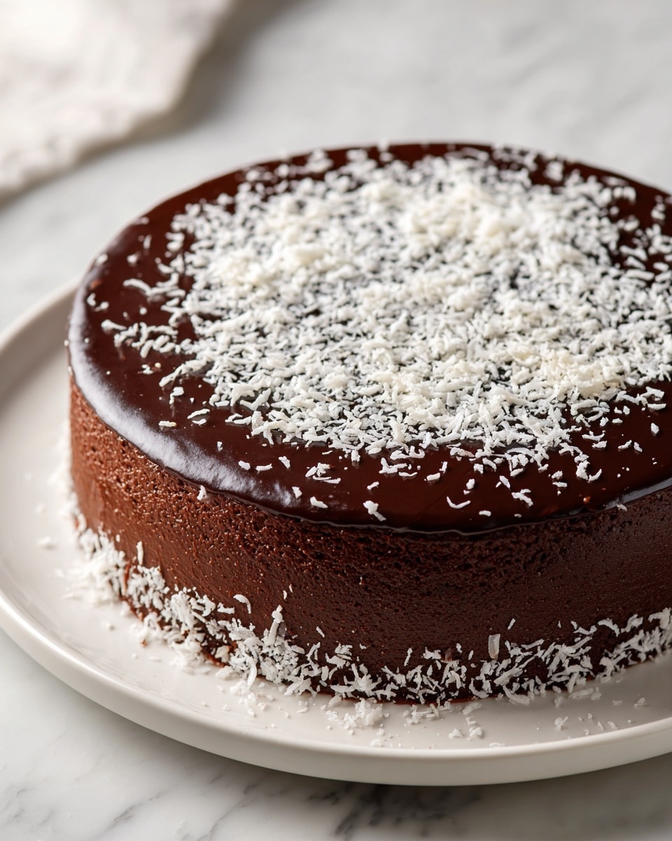 A round chocolate cake with a smooth, dark glossy top layer covered with a light sprinkle of white shredded coconut in the center and around the base. The cake is on a white plate against a white marbled surface, showing clean edges and an even, thick chocolate layer all around. The texture of the top layer looks shiny and firm, while the sides have a matte finish. photo taken with an iphone --ar 4:5 --v 7
