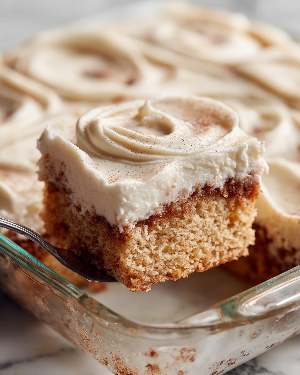 A close-up image of a square piece of cinnamon roll cake being lifted from a clear glass baking dish. The cake has two main parts: the bottom part is a light tan and beige swirl pattern showing cinnamon inside the soft, fluffy cake, and the top part is a thick, creamy, smooth layer of white frosting with swirled texture, spread evenly covering the whole cake. The background is a white marbled surface. Photo taken with an iphone --ar 4:5 --v 7
