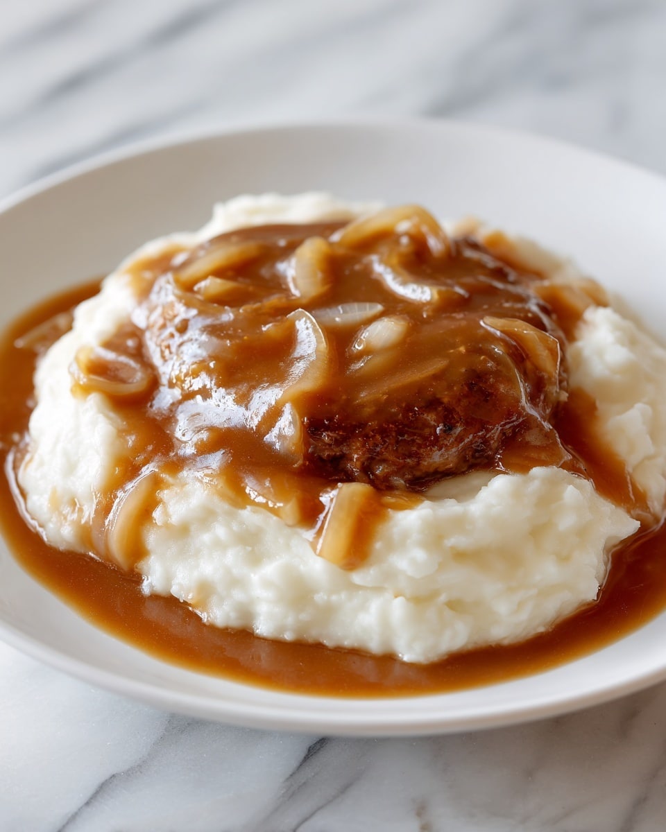 The dish shows one layer of creamy, smooth off-white mashed potatoes spread on a white plate with a slightly uneven surface. On top of the potatoes is a single brown meat patty covered in a thick, shiny brown gravy. The gravy is glossy and has visible soft, translucent cooked onion rings spread over the meat and slightly spilling onto the mashed potatoes around the edges. The dish is placed on a white marbled texture surface. photo taken with an iphone --ar 4:5 --v 7