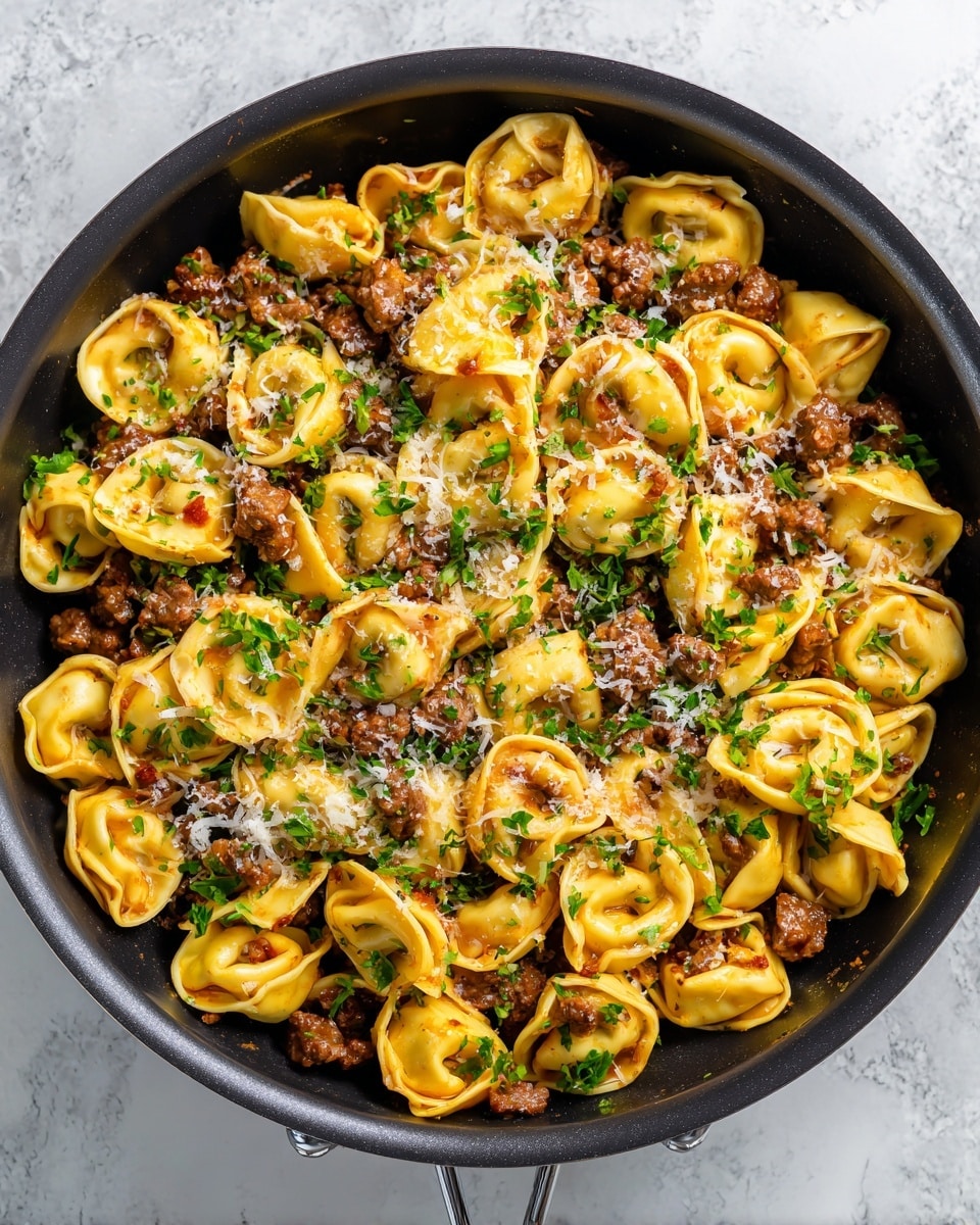 A black pan filled with round, yellow tortellini pasta arranged all over the pan, mixed with thick, browned beef pieces placed randomly on top and between the pasta. The dish is covered with small green parsley flakes scattered evenly, and there are light white grated cheese bits sprinkled over the whole mix. The pan is on a white marbled textured surface. photo taken with an iphone --ar 4:5 --v 7