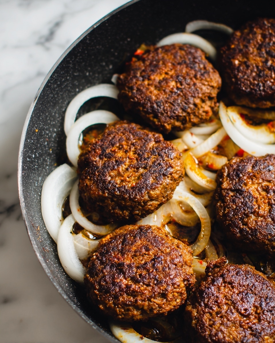 The image shows a dark cooking pot filled with several browned meat patties with a rough texture, some round and some more oval shaped, laying over thin slices of pale white onion rings that create a base layer. The patties have a rich dark brown color with bits of orange and red visible, indicating spices, and some shine from cooked juices. The pot itself is dark and contrasts with the light onion underneath the patties. The background is a white marbled texture. photo taken with an iphone --ar 4:5 --v 7