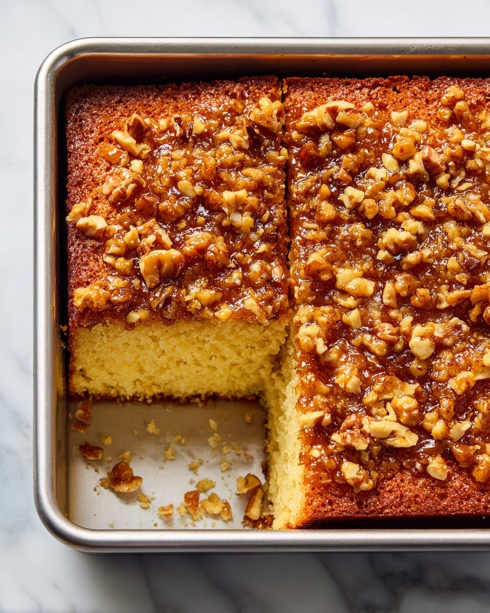 A close-up view of a square piece of yellow cake with a crumbly, moist texture, held by a silver spatula above a large dark baking tray filled with the rest of the cake. The cake has two layers: a thick bottom layer that is soft and yellow, and a thick top layer made of a glossy, brown nutty topping with a sticky, textured surface from chopped nuts evenly spread. The background is dark, and a light blue and white checkered cloth is partly visible under the baking tray. photo taken with an iphone --ar 4:5 --v 7