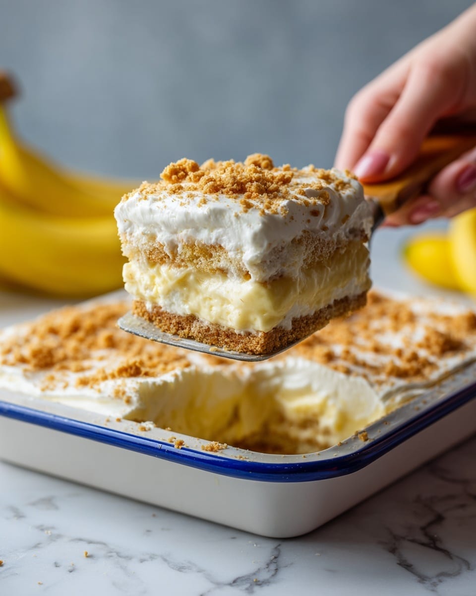 A square slice of layered dessert being lifted by a woman's hand using a spatula, showing four visible layers of golden-brown cracker or cookie separated by three creamy light yellow custard or pudding layers, topped with a thick, smooth white whipped cream layer sprinkled with light brown crumbs. The dessert is placed in a white baking dish with blue edges on a white marbled surface, with a yellow banana blurred in the background. Photo taken with an iphone --ar 4:5 --v 7