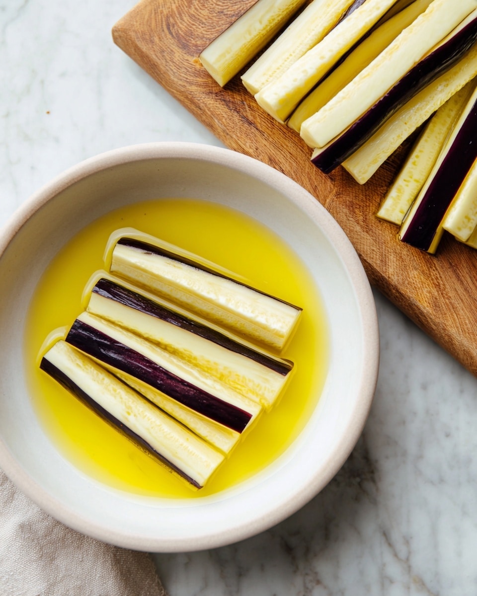 In the image, there is a white bowl holding five long slices of pale yellow eggplant with dark purple edges, partially covered in a bright yellow liquid mixture, placed on a white marbled surface. Behind the bowl, a wooden cutting board holds many more similar long slices of eggplant stacked loosely. The scene is simple and clean, with soft natural lighting that highlights the textures and colors of the eggplant and the liquid. Photo taken with an iphone --ar 4:5 --v 7