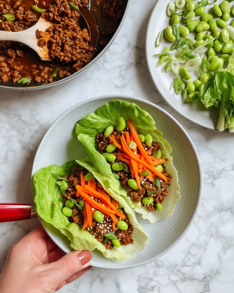 The image shows a white bowl with two light green lettuce leaves used as wraps. Inside each leaf, there is a layer of cooked ground meat in a thick brown sauce at the bottom. On top, there is a layer of bright orange carrot sticks and vibrant green edamame beans, sprinkled with white sesame seeds and small green onion pieces. To the upper right, there is a white plate with more green edamame beans, sliced green onions, and extra orange carrot sticks. On the right side, there is a small pile of fresh lettuce leaves. The background is a white marbled texture. A woman's hand is holding a red spoon inside a pan with the same cooked ground meat in brown sauce. Photo taken with an iphone --ar 4:5 --v 7
