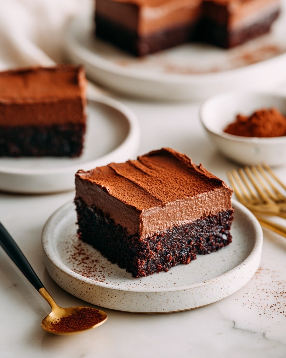 A square-shaped two-layer chocolate dessert sits on a small white speckled plate placed on a white marbled surface. The bottom layer is dark, dense, and crumbly, while the top layer is thick, smooth chocolate frosting with a slightly textured surface and soft ridges along the edges. To the left, there is a gold spoon with a black handle resting on the surface, holding some of the smooth chocolate topping. In the background, there is a small white bowl filled with cocoa powder and parts of other similar dessert pieces on matching plates. Three gold forks lie flat on the right side of the surface. Photo taken with an iphone --ar 4:5 --v 7