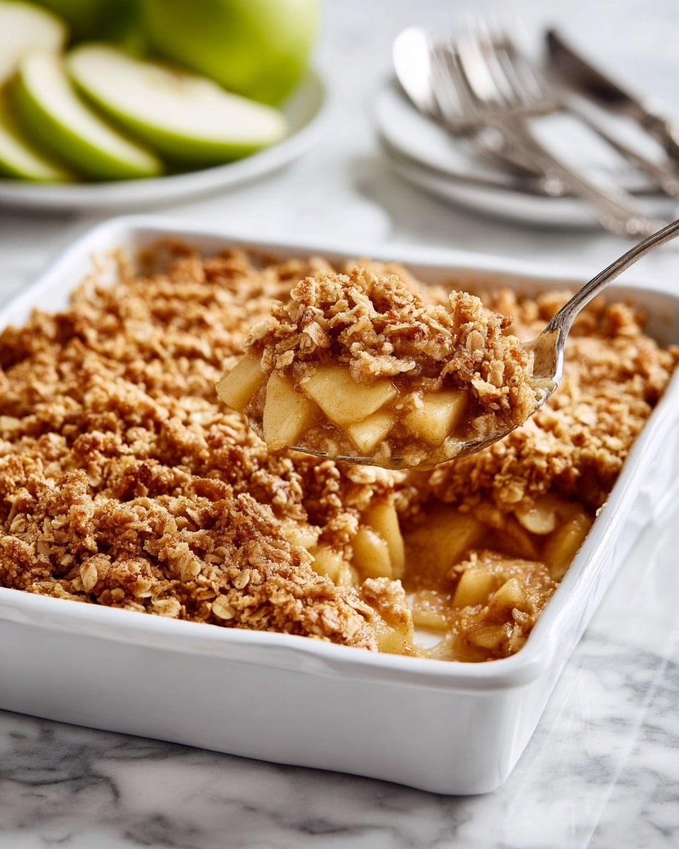 A white rectangular baking dish filled with a layered apple crisp dessert is shown on a white marbled surface. The bottom layer is made of soft, cooked apple pieces in light golden color with a slightly shiny texture, visible on a spoon lifting a portion from the dish. The top layer is a thick, crumbly oat and brown sugar mixture, golden brown with a rough texture of small clusters. In the background on the white marbled surface are sliced green apples and a white plate with silver forks. The photo is taken with an iphone --ar 4:5 --v 7