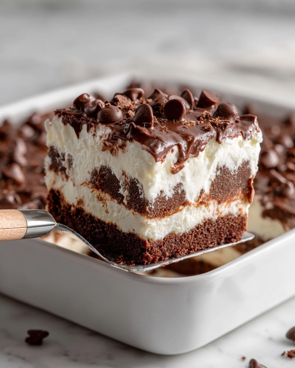 The image shows a close-up of a thick square piece of dessert with three visible layers: a bottom brown cake-like layer, a middle creamy white layer, and a top layer scattered with shiny milk chocolate chips, some embedded and others on the surface. The edges look soft and slightly crumbly. The dessert sits in a white rectangular pan on a white marbled surface. A metal spatula with a light wooden handle is lifting the piece slightly from the pan. The texture looks moist and rich, with a mix of smooth cream and soft cake. Photo taken with an iphone --ar 4:5 --v 7