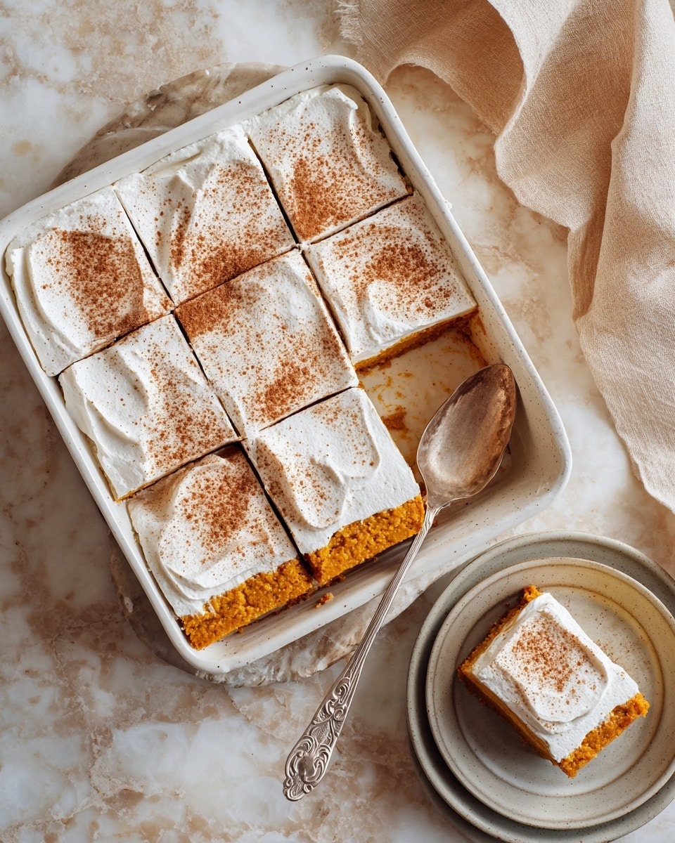 A white ceramic rectangular dish holds a pumpkin dessert cut into six equal squares. The dessert has two main layers: a thick orange pumpkin base with a moist texture, and a smooth white cream layer on top that is evenly spread and dusted with a fine layer of cinnamon powder, adding a light brown color. One square is missing, showing the side of the pumpkin layer, while an ornate metal serving spoon lies in the empty space. A slice of the dessert is placed on a light gray plate nearby. The whole scene is set on a white marbled surface with a warm, cozy feel. photo taken with an iphone --ar 4:5 --v 7