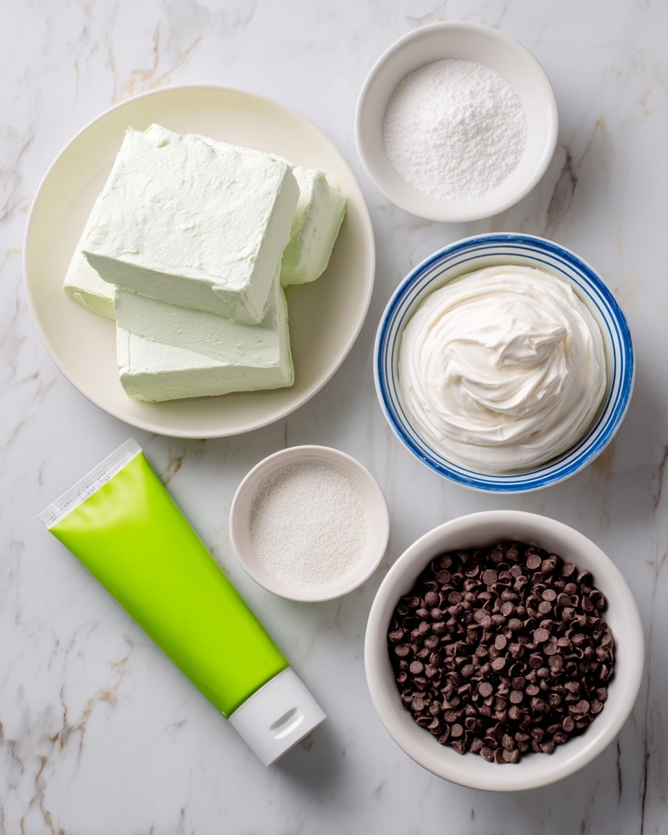 Several white bowls and a small white plate sit on a white marbled surface. One white bowl is filled with three thick, creamy white blocks of cream cheese. Another white bowl holds a smooth, soft white whipped topping. A third white bowl contains a fine white powder of confectioners sugar. A small white plate is empty. Nearby, a tube of bright green food coloring lies flat on the marbled surface, and a white bowl with a blue rim is filled with small, dark brown mini chocolate chips. Each item is clearly labeled with bold black text. Photo taken with an iphone --ar 4:5 --v 7